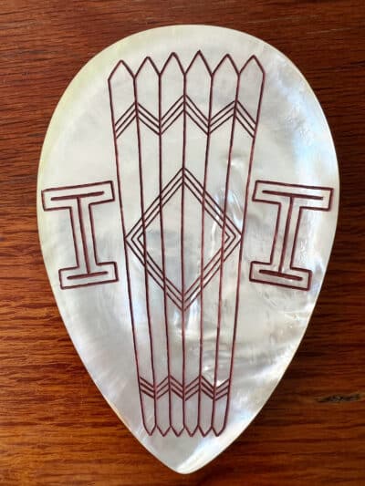 Mother of pearl in tear drop shape, etched with symbols in native designs.