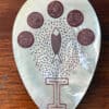 Mother of pearl in tear drop shape, etched with 5 circles at the top and a fish in the middle.